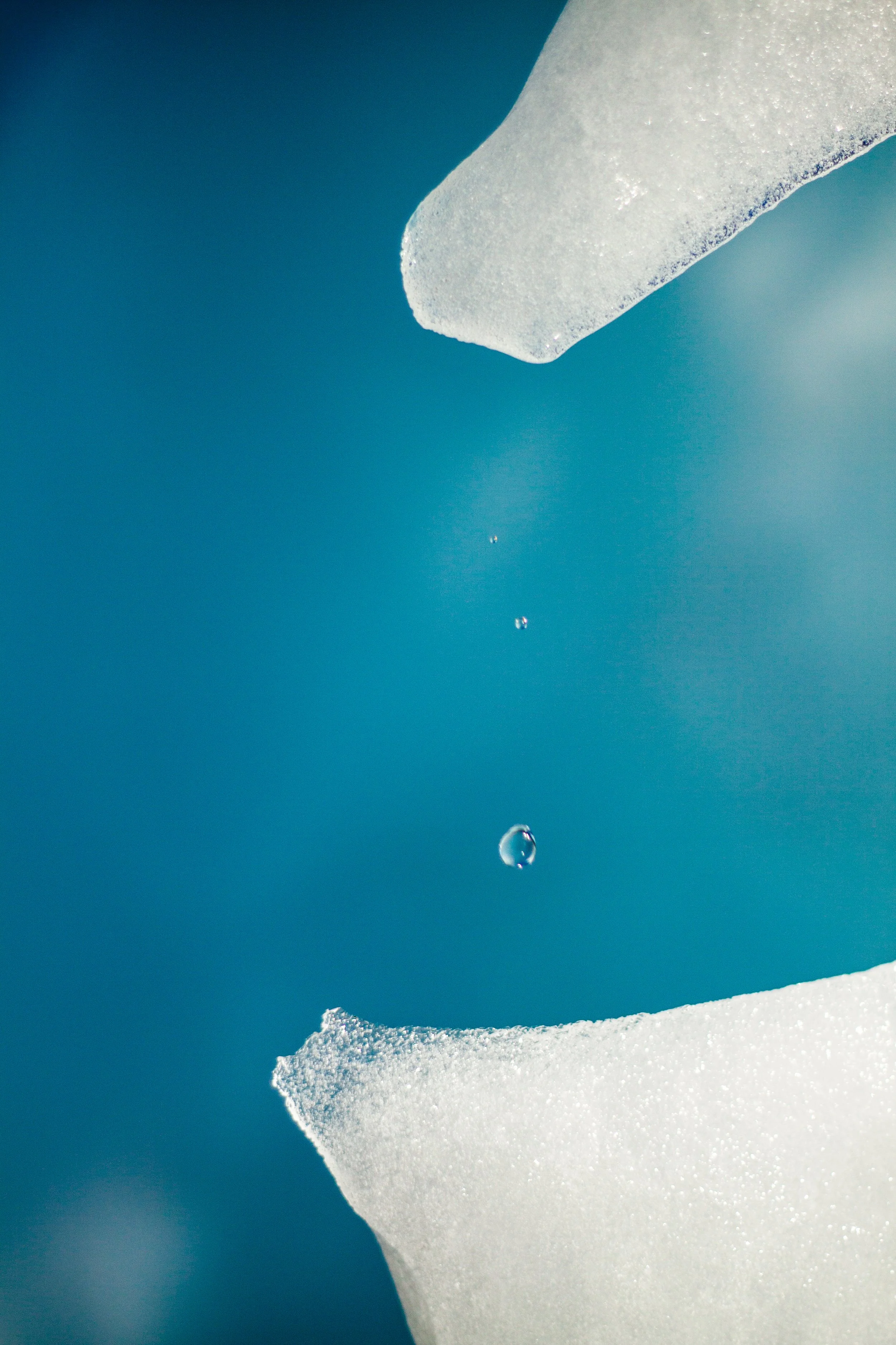Nahaufnahme von Eissplittern mit Wassertröpfchen zwischen ihnen gegen blauen Hintergrund.
