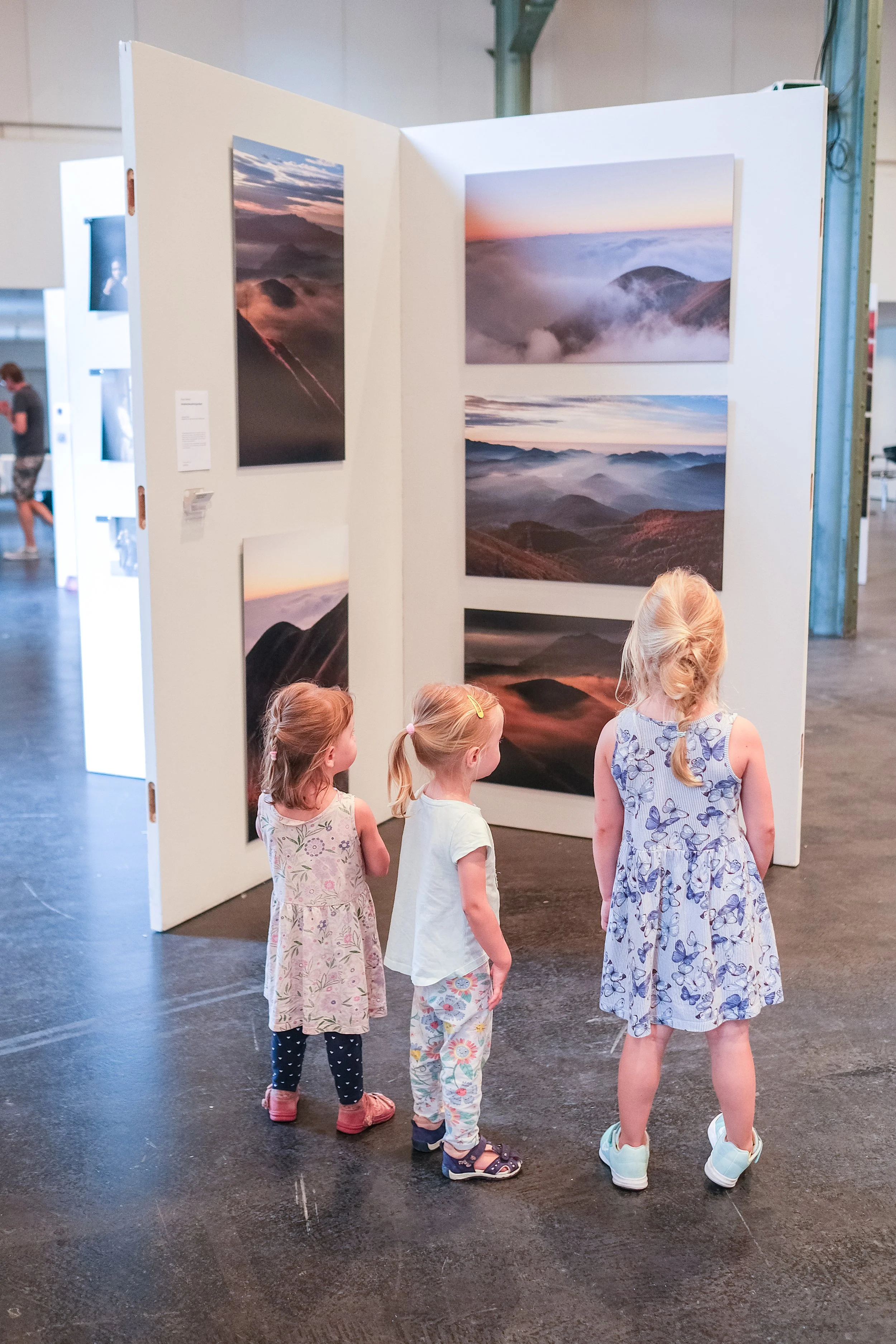 Drei kleine Mädchen betrachten eine Kunstausstellung mit Landschaftsfotografien in einem Museum.