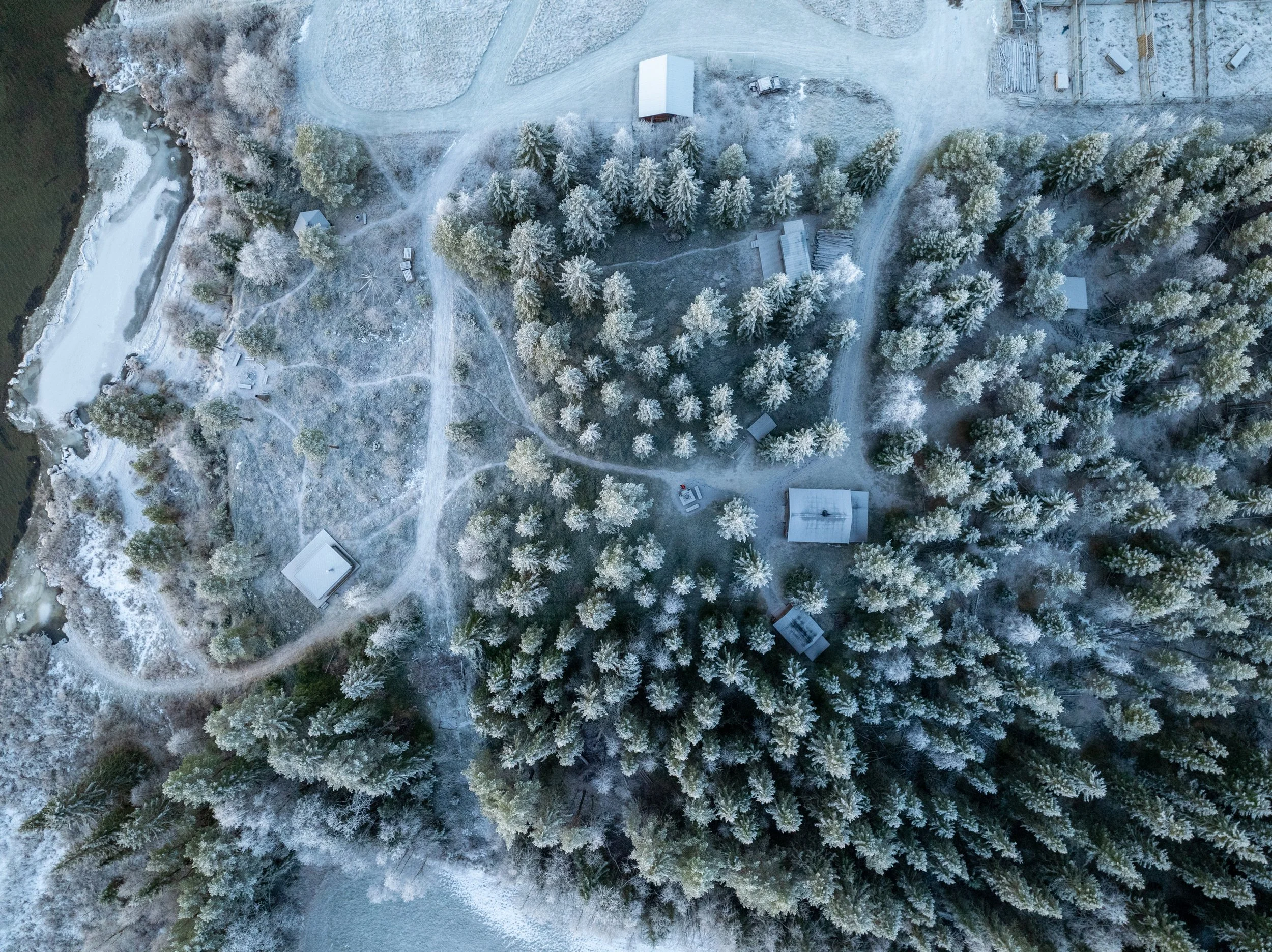 Vogelperspektive auf eine verschneite, bewaldete Landschaft mit Wegen, kleinen Gebäuden und einem kleinen Teich