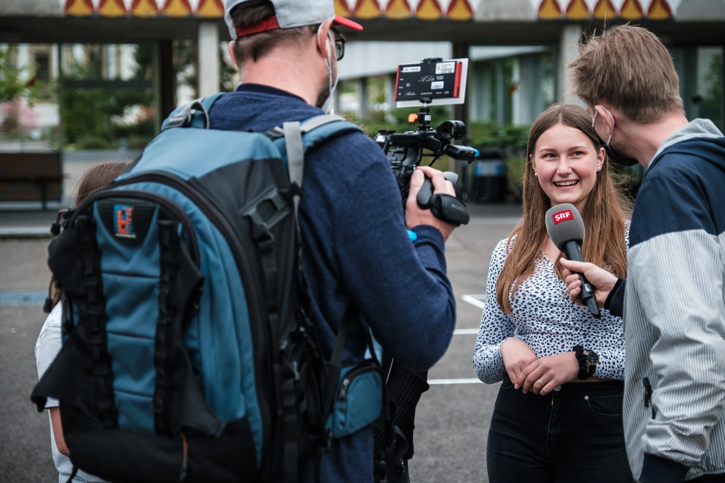 Mädchen wird von Journalisten interviewt, während sie ein Mikrofon hält, draußen.