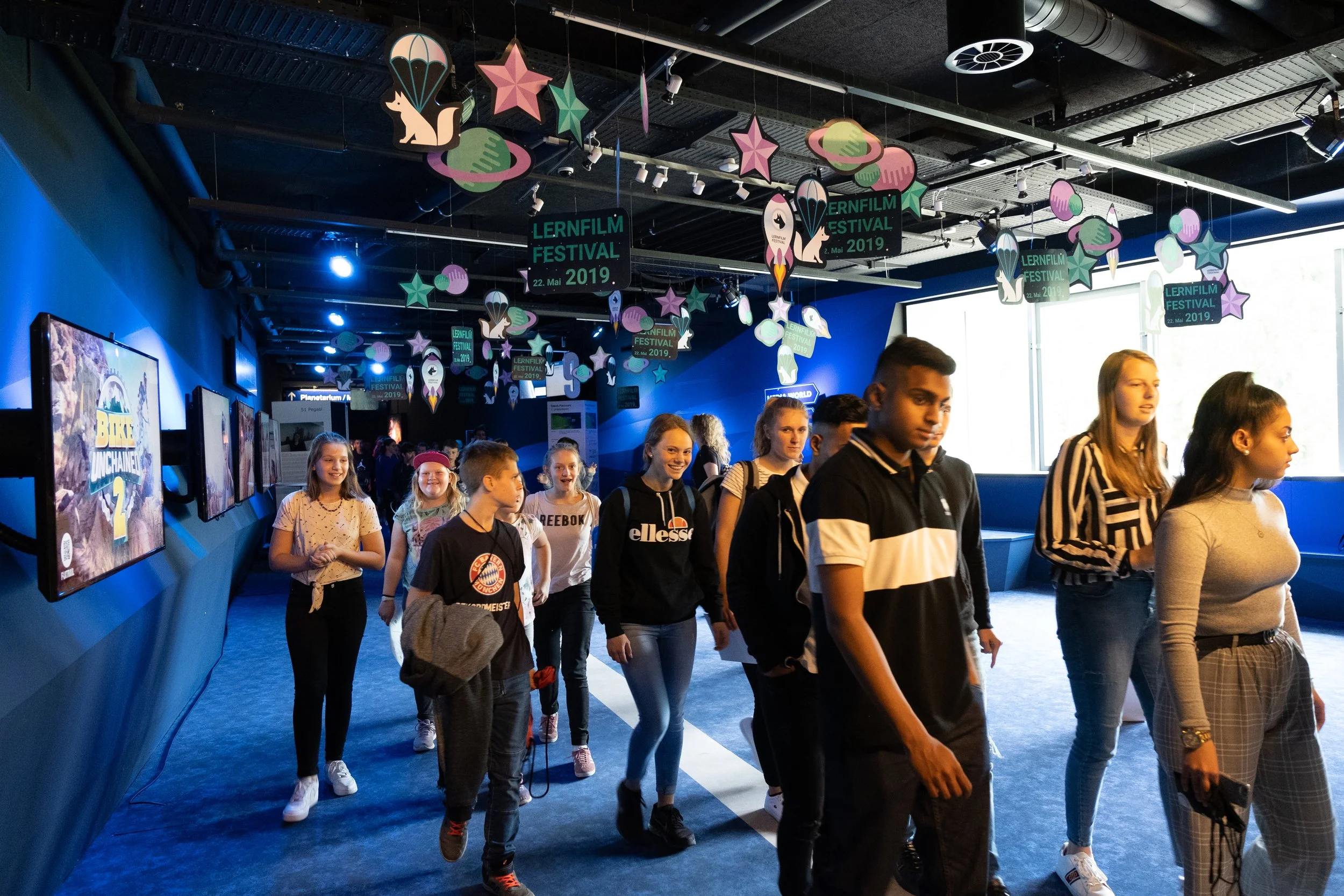 Junge Menschen in einer moderner Ausstellunghalle, die den Lernfilmfestival 2019 feiert, mit Dekorationen und Displays.