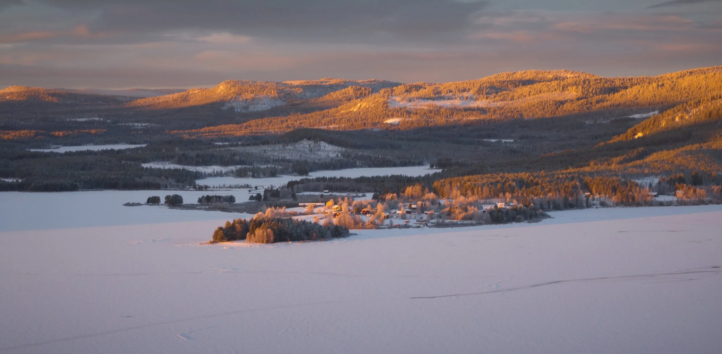 Schneebedeckter Landschaft mit kleinen Häusern und Wäldern, im Sonnenuntergang