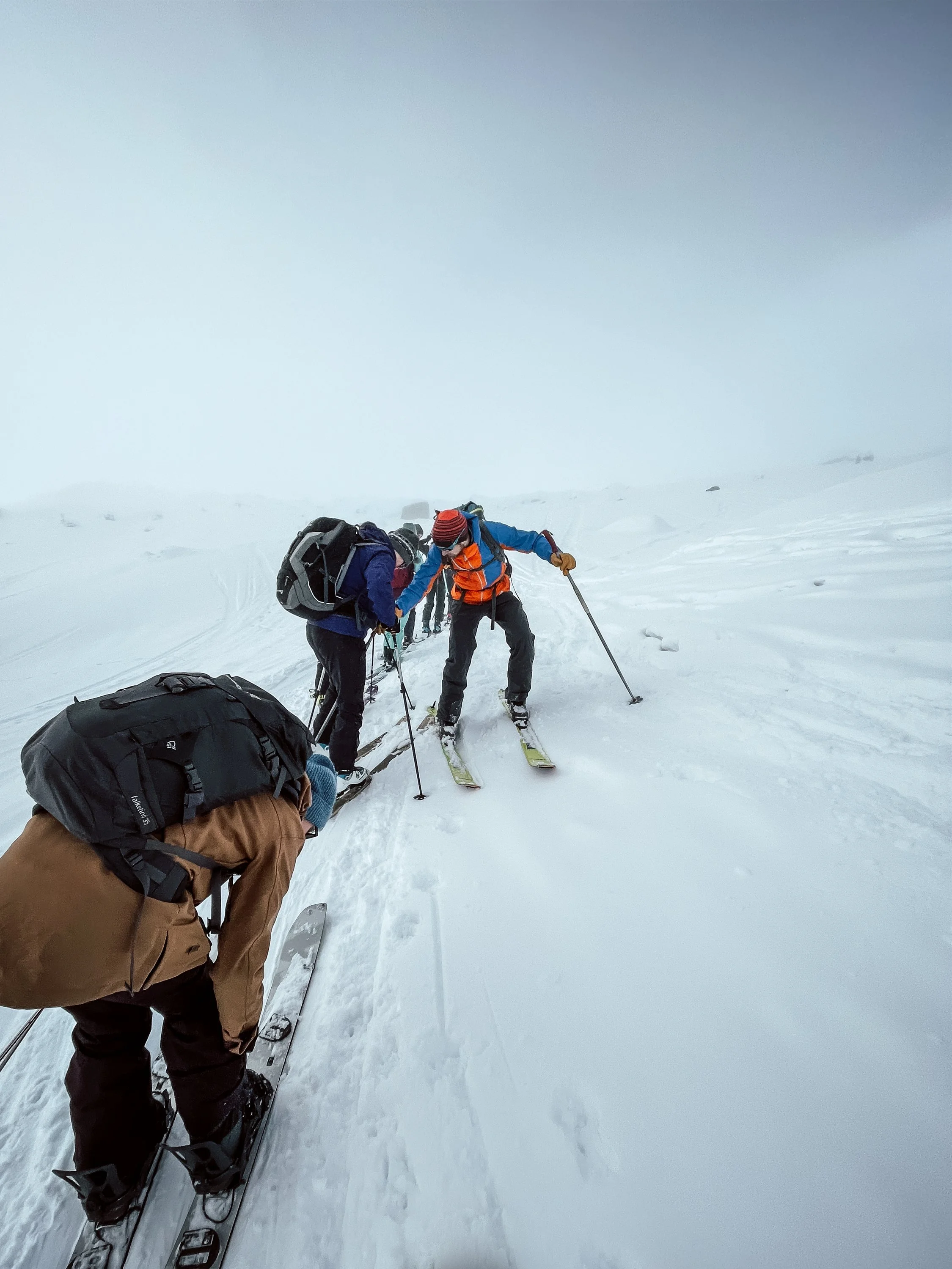 Gruppe von Skifahrern in Schneelandschaft bei schlechtem Wetter oder Nebel, einige helfen sich gegenseitig.