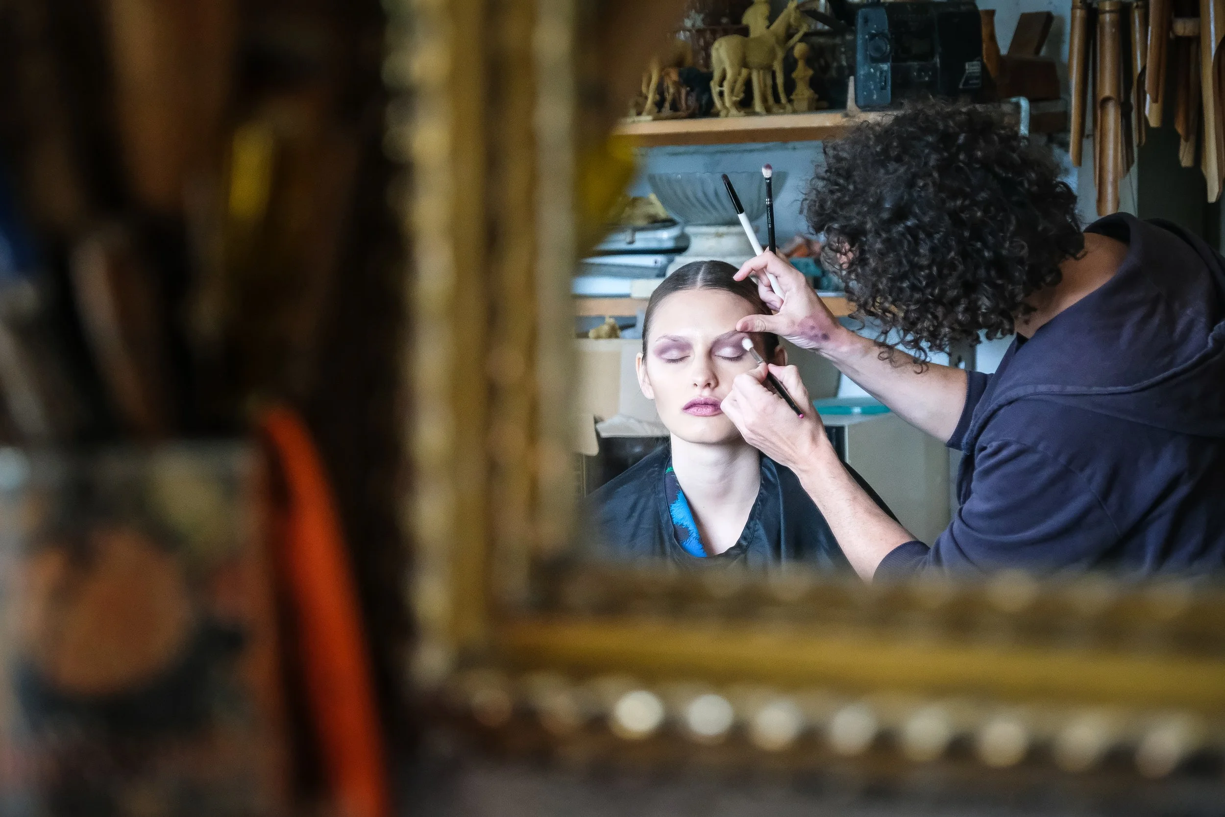 Friseur arbeitet an Make-up einer Frau in einem Salon, Blick durch einen Spiegel
