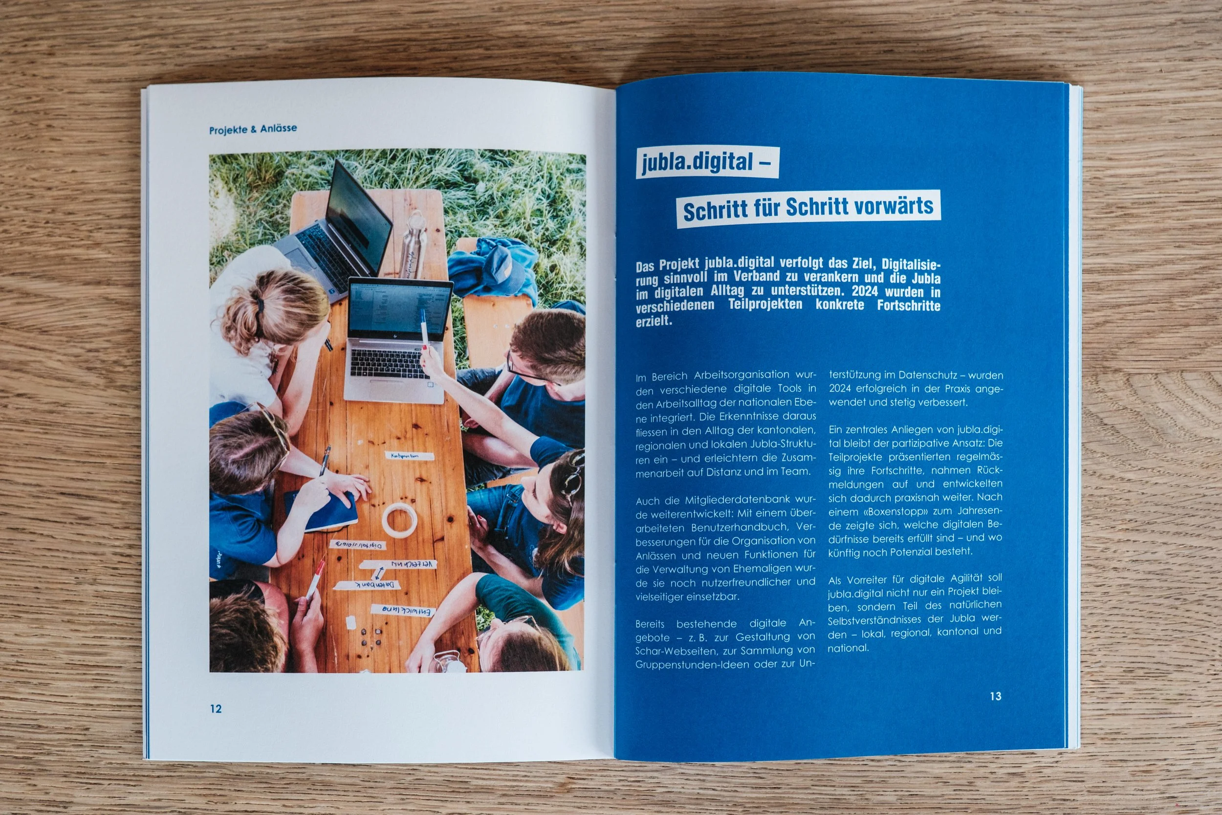 Offen gebaute Broschüre mit Text und Bild, links ein Foto von mehreren Kinder im Freien, die an einem Holztisch mit Laptops und Schreibmaterial arbeiten, rechts blauer Hintergrund mit weißen Text.