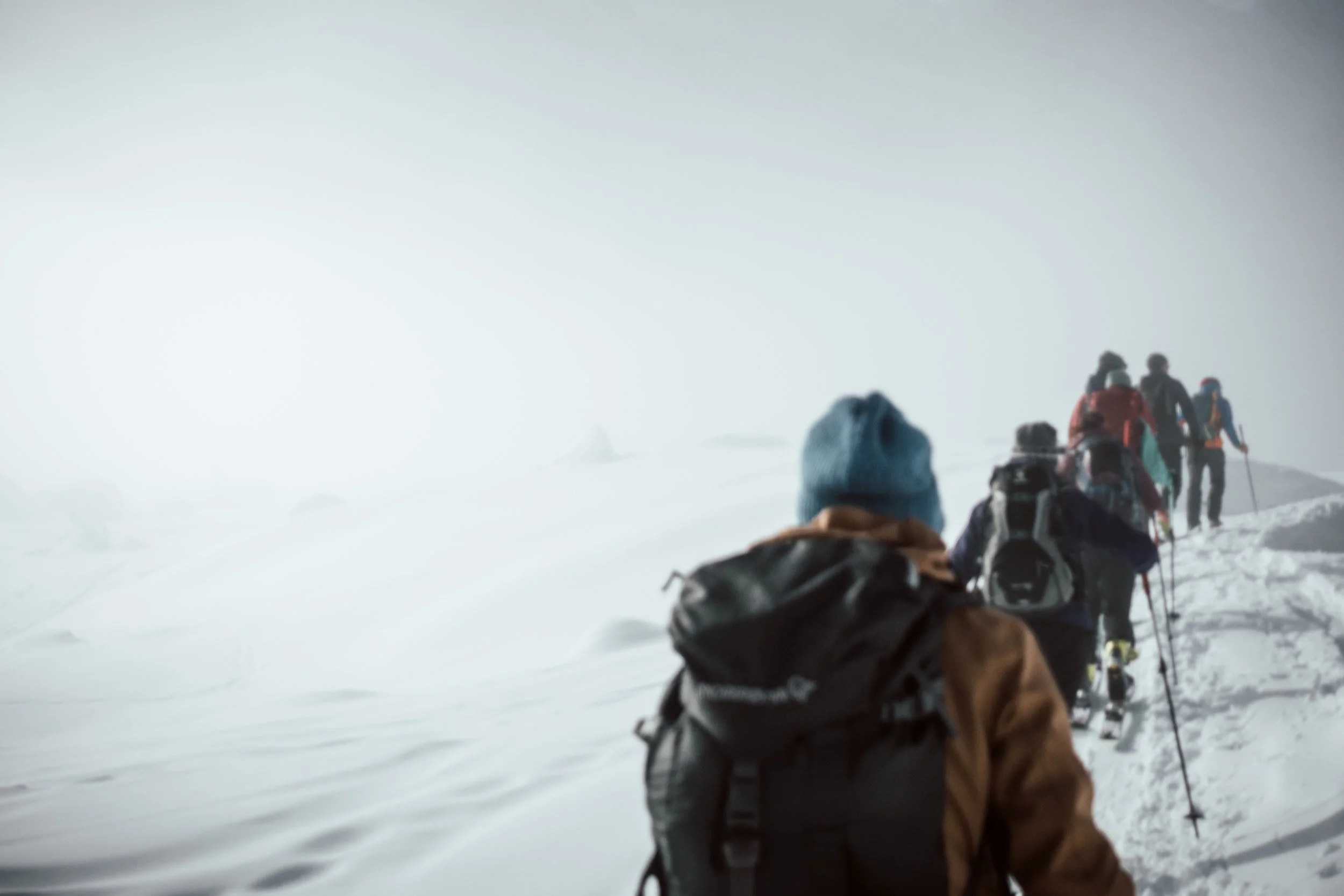 Eine Gruppe von Schneeschuhwanderern in Winterkleidung und mit Rucksäcken wandert durch eine verschneite, neblige Berglandschaft.