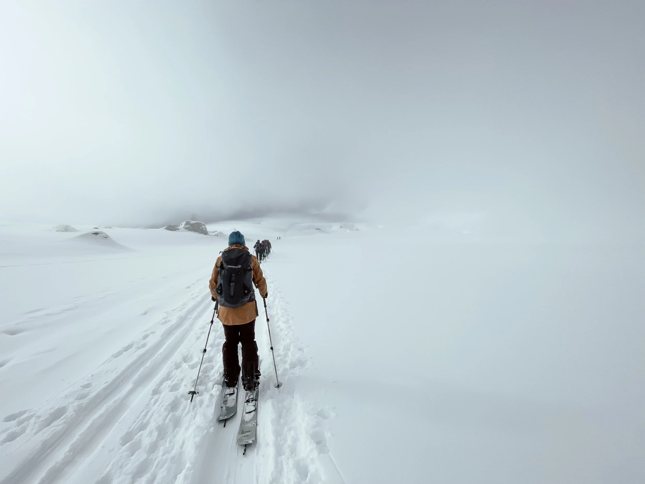 Skifahrer auf schneebedecktem Gelände in nebliger Berglandschaft.