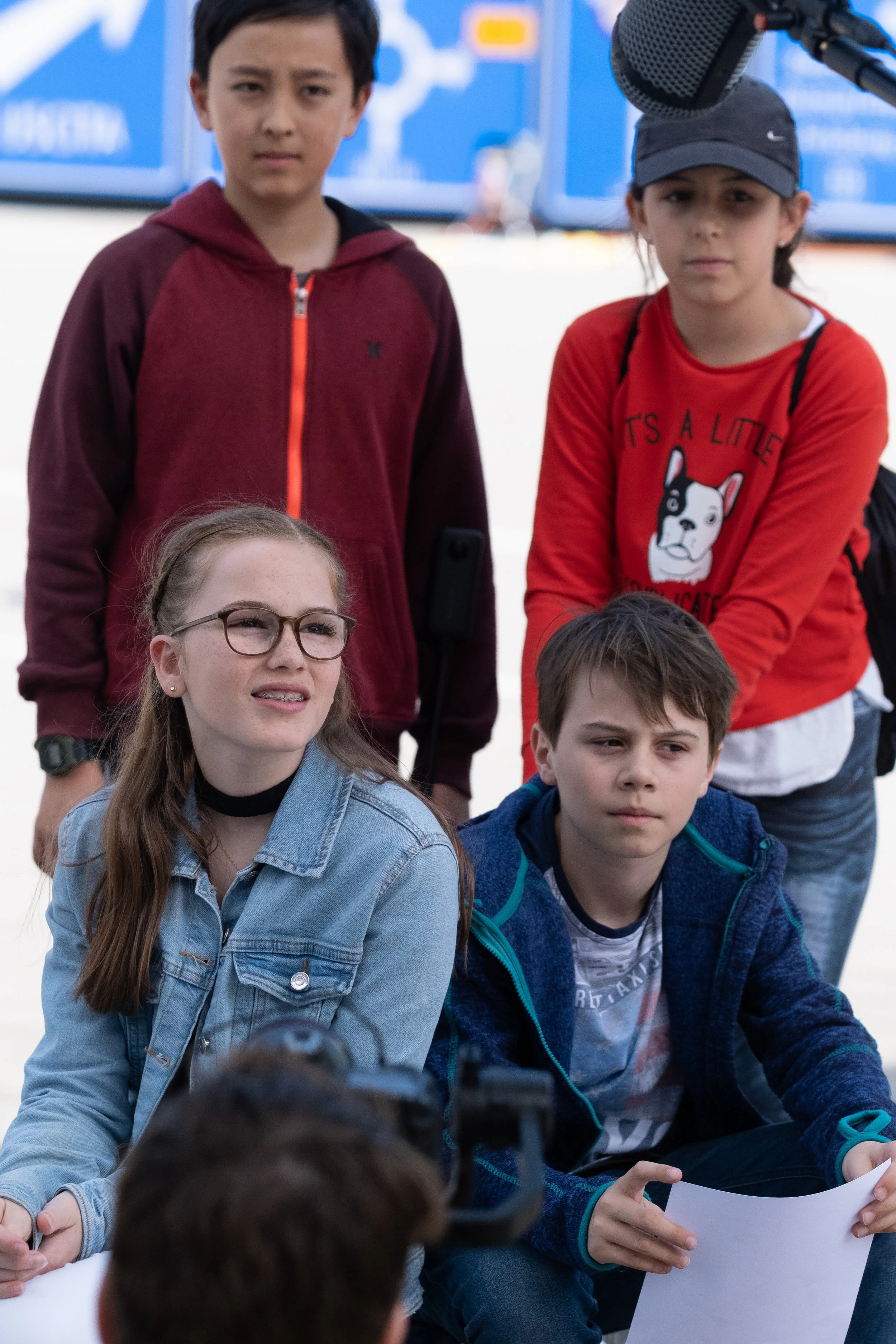 Fünf Kinder sitzen und stehen bei einem Interview im Freien, mit Kamera und Mikrofon, während sie Fragen beantworten.