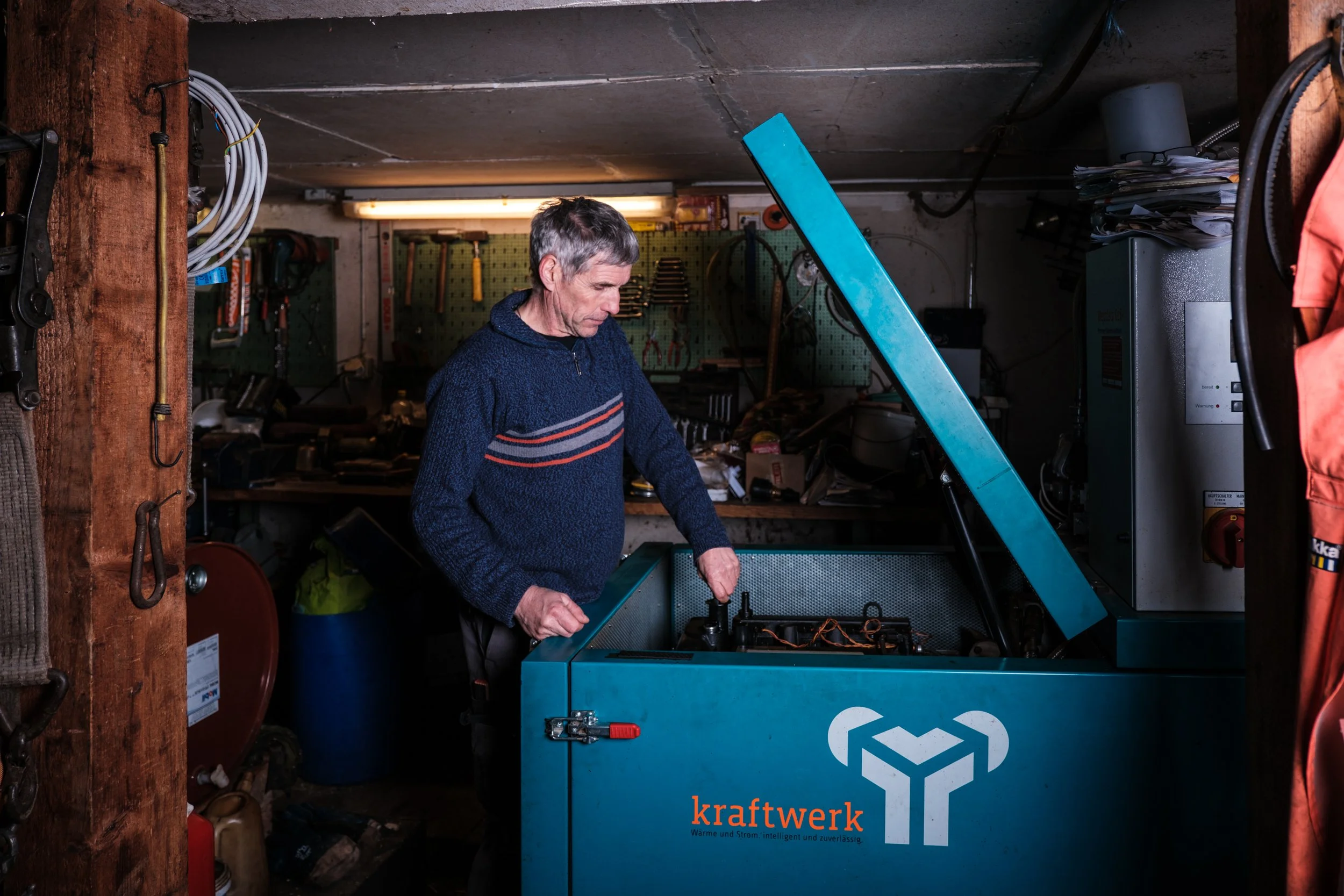 Ein älterer Mann arbeitet in einer Werkstatt an einem blauen Kaltwassergerät mit dem Schild 'kraftwerk'.