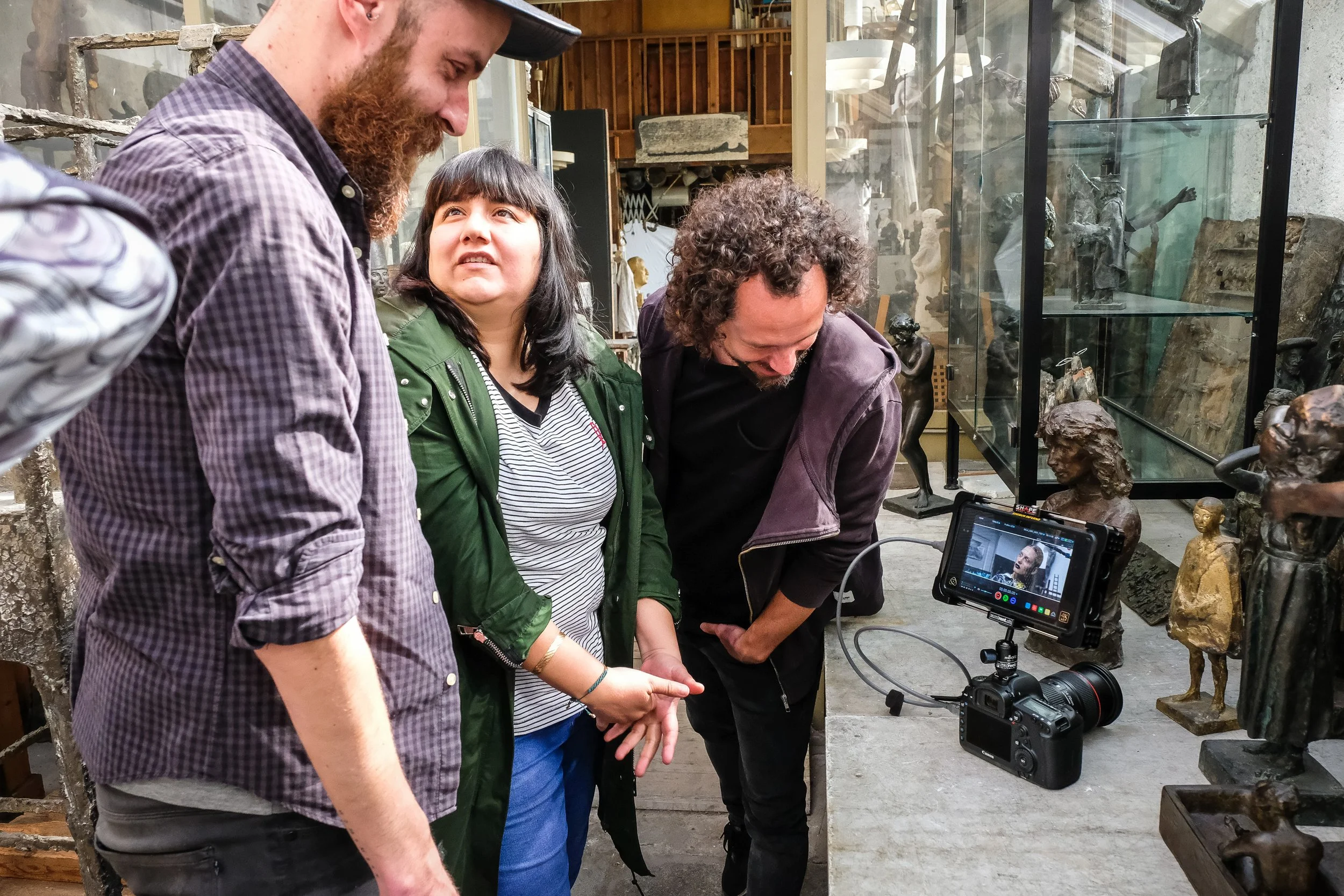 Drei Menschen beim Filmdreh in einem Museum mit Skulpturen, eine Kamera filmt die Szene.