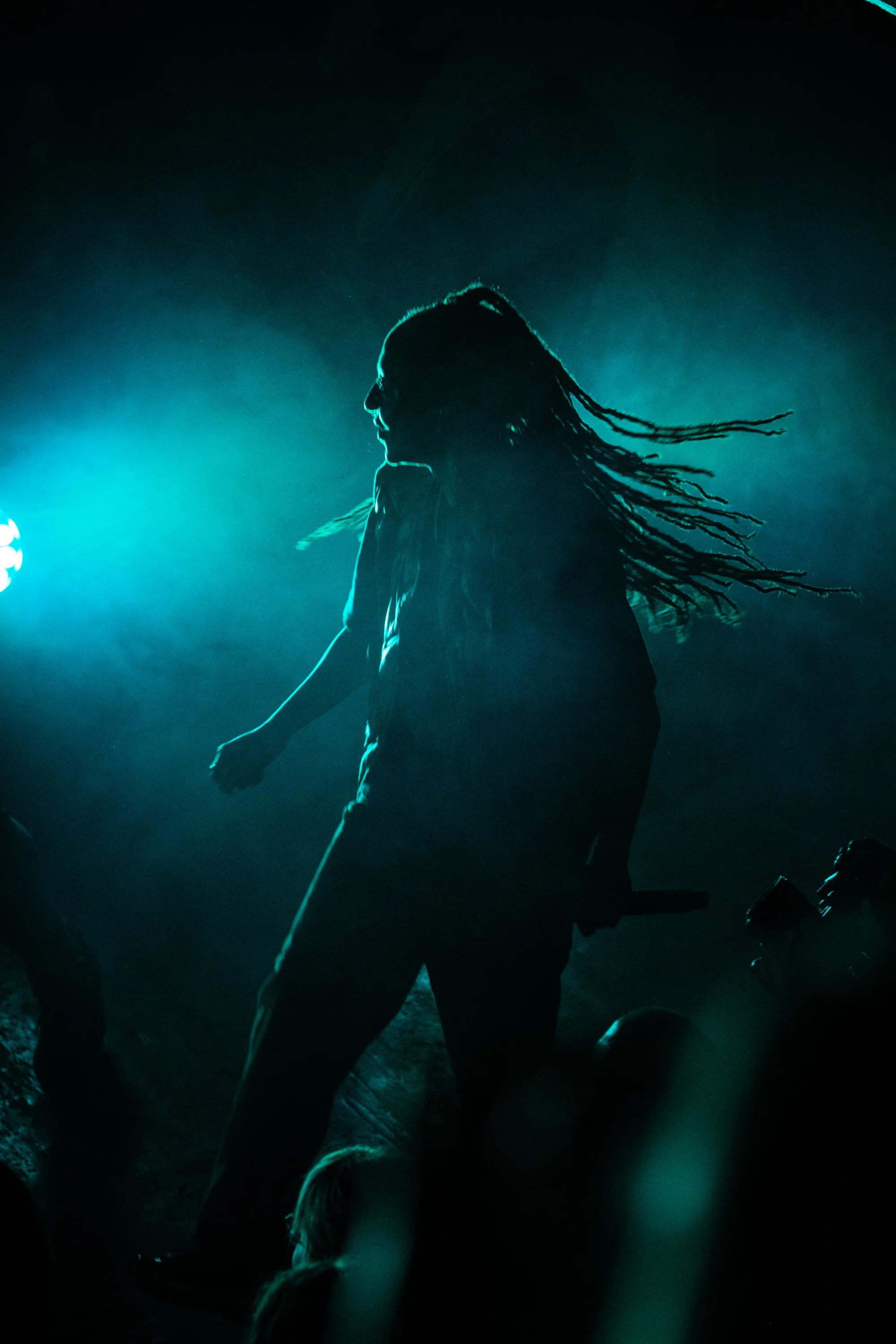 Silhouette eines Menschen mit dreadlocks bei Dunkelheit, beleuchtet von bläulichem Licht.