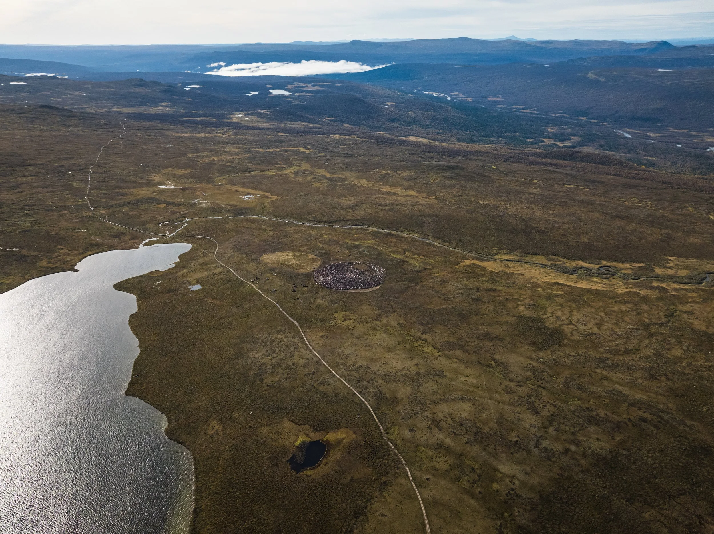 Landschaft mit See, Wanderweg, Felsen und Bergen im Hintergrund in der Ferne.