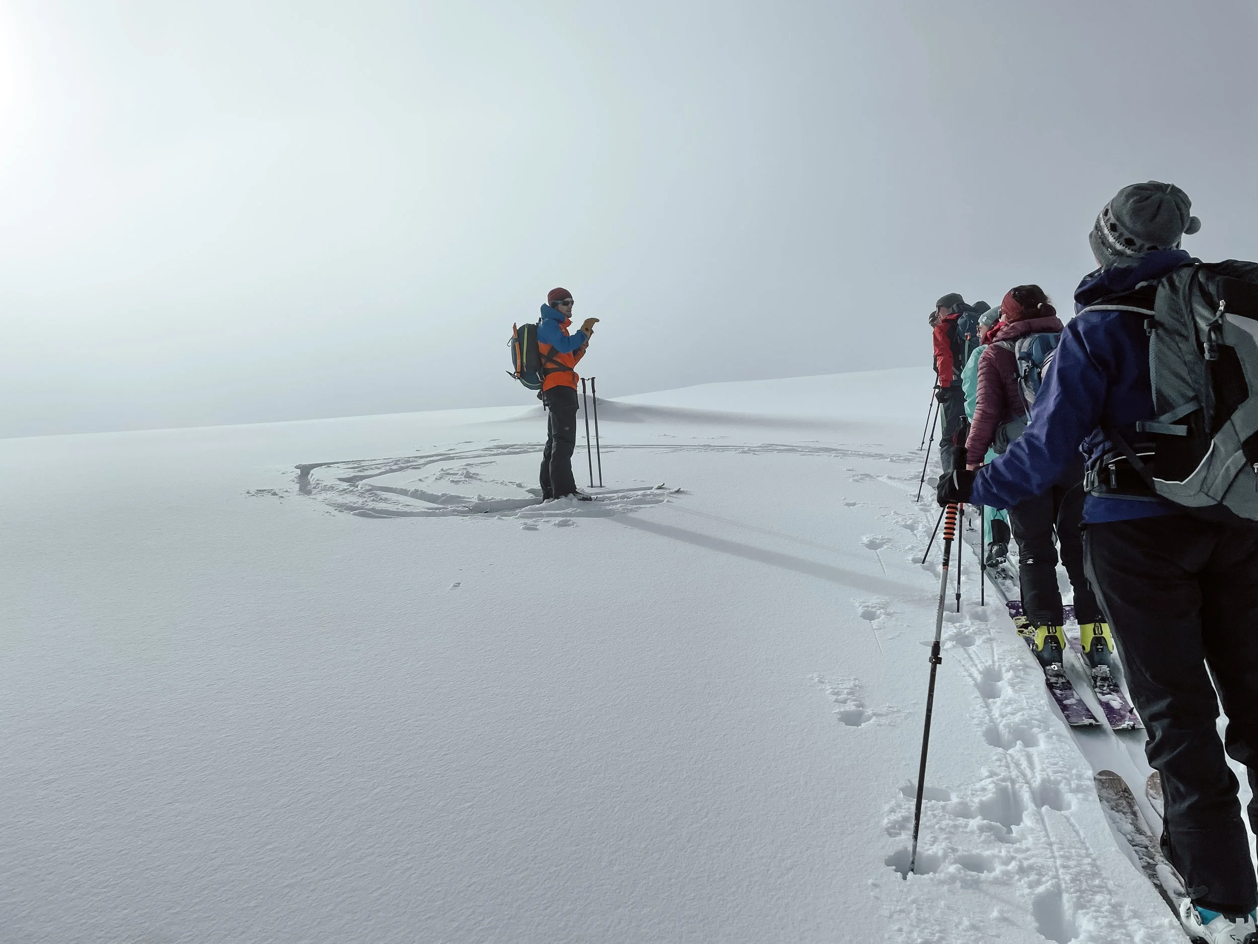 Gruppe von Skiwanderern in verschneiter Berglandschaft, einer liest eine Karte, andere warten in einer Reihe.