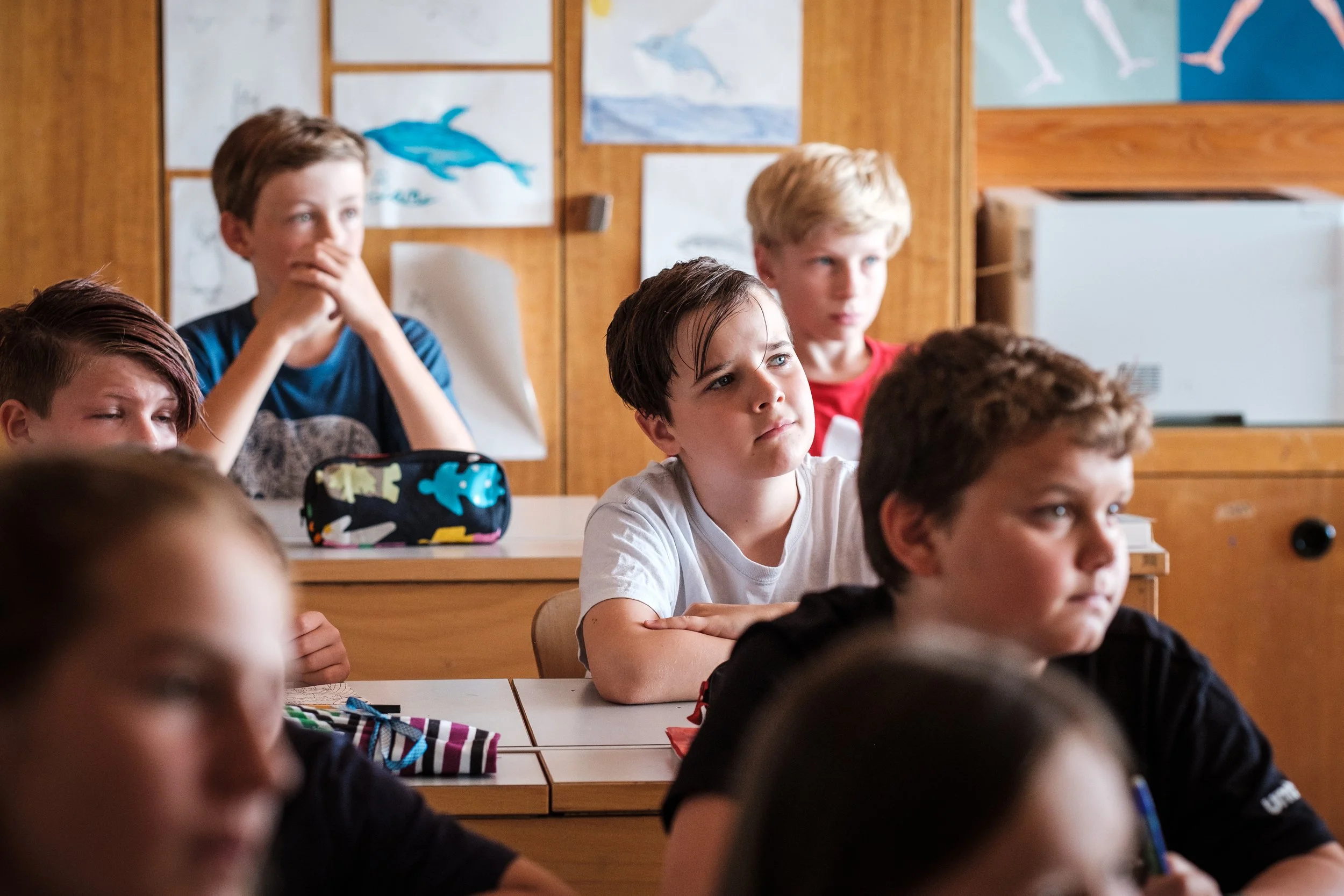 Schüler in einer Klasse, die aufmerksam einem Lehrer zuhören, mit Bildern von Meerestieren an der Wand.