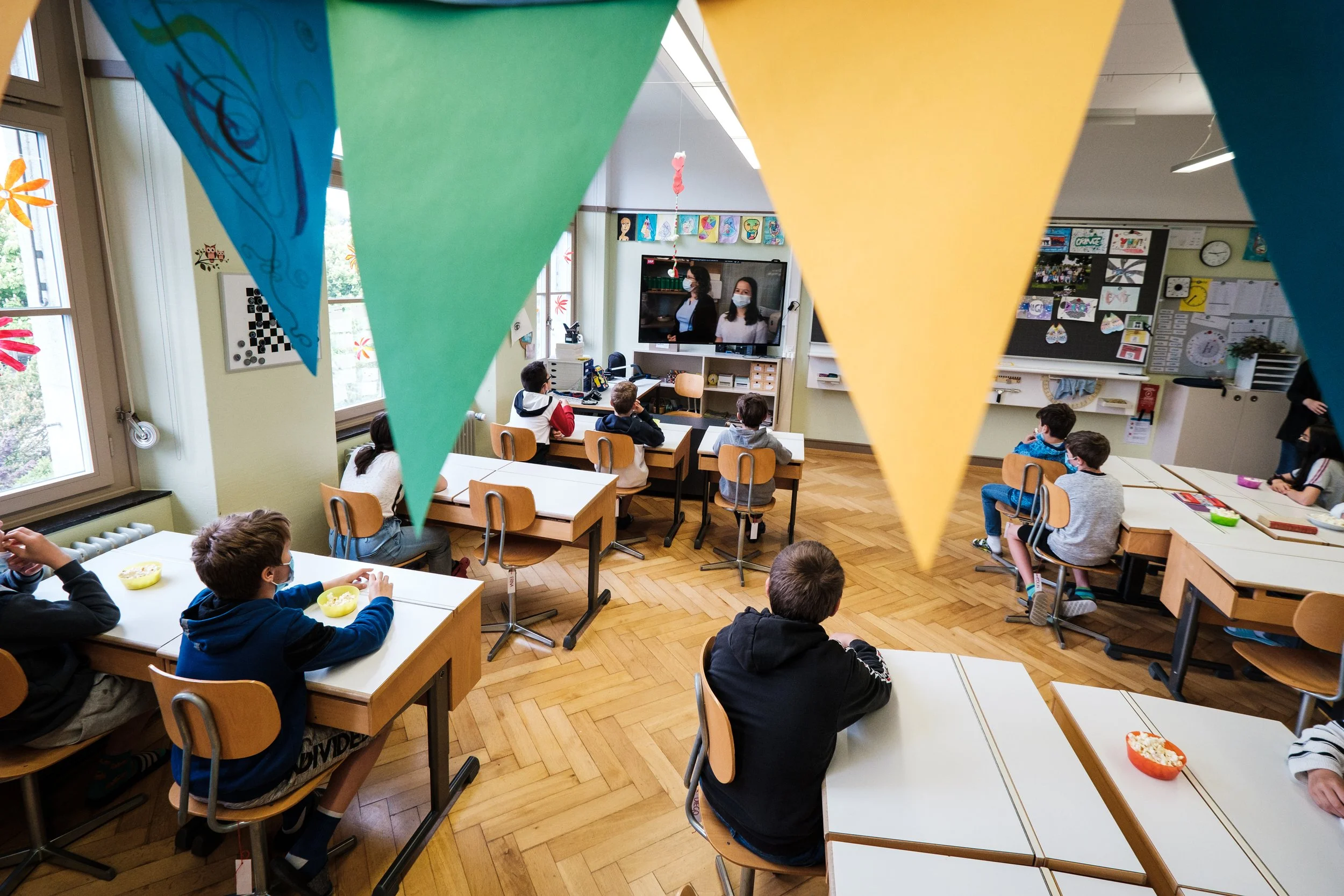 Grundschule Klassenzimmer mit Kindern, die Fernseher schauen, farbige Wimpel im Vordergrund, Kunstwerke an den Wänden.