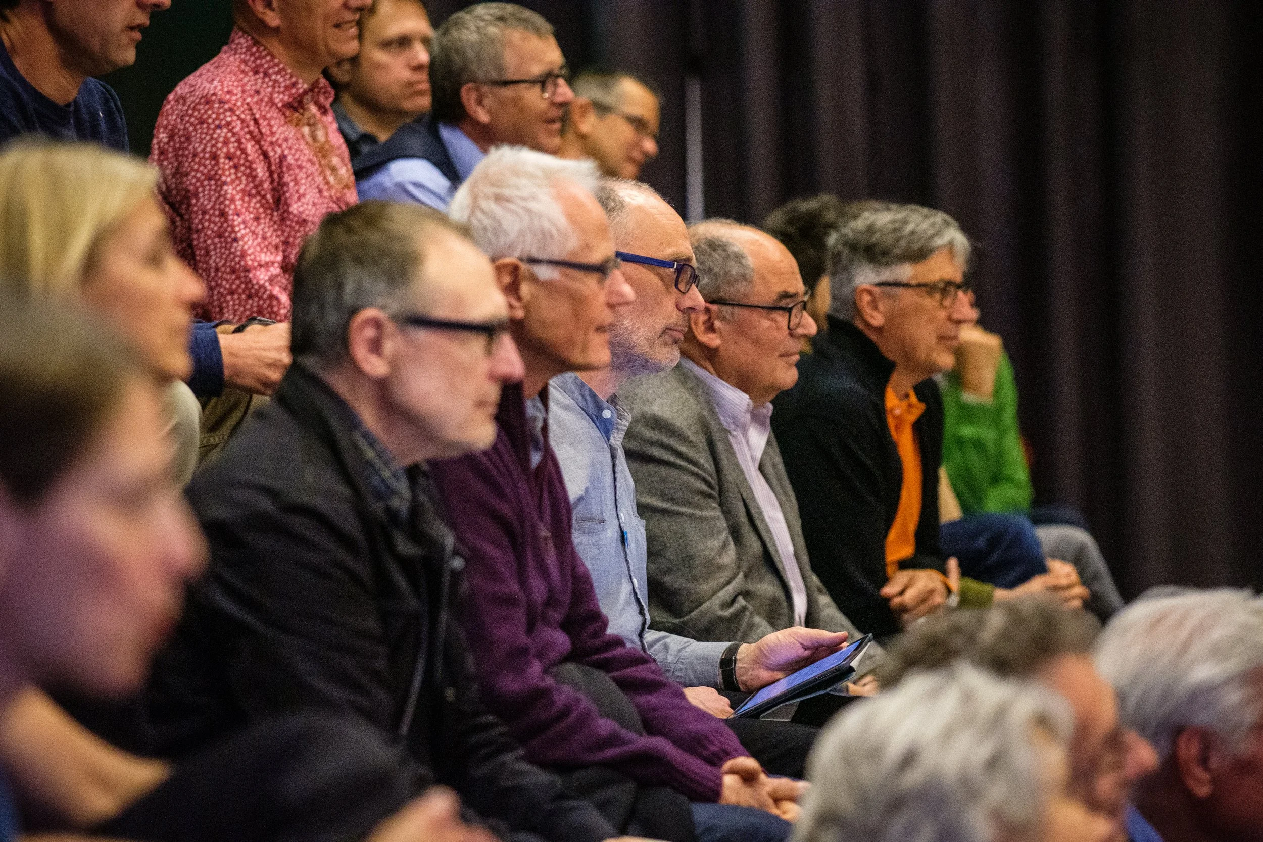 Mehrere Menschen sitzen und schauen aufmerksam bei einer Veranstaltung in einem dunklen Raum.