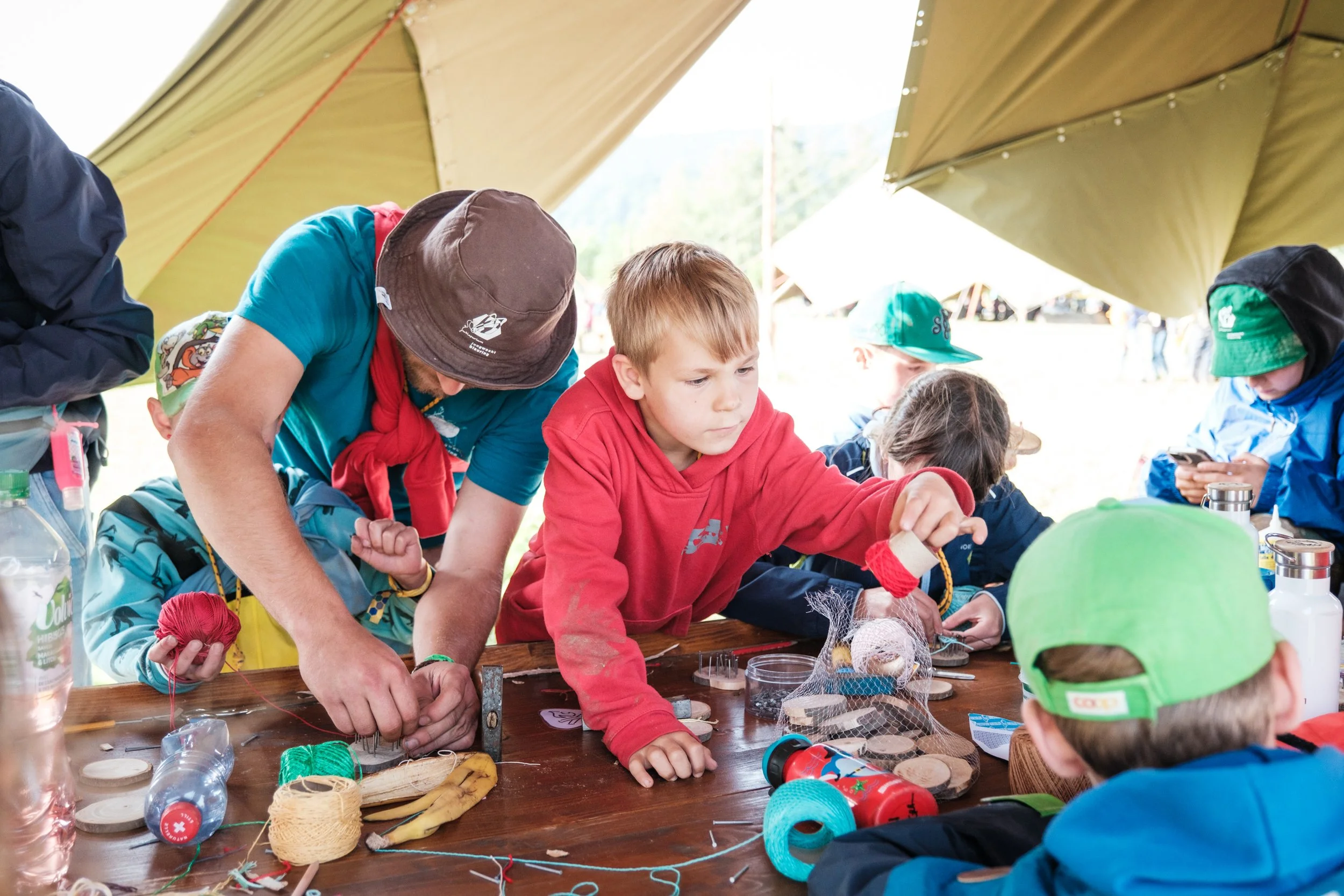 Kinder und Erwachsener arbeiten gemeinsam an einem Bastelprojekt unter einer großen Zeltdach, mit Bastelmaterialien auf einem Tisch.