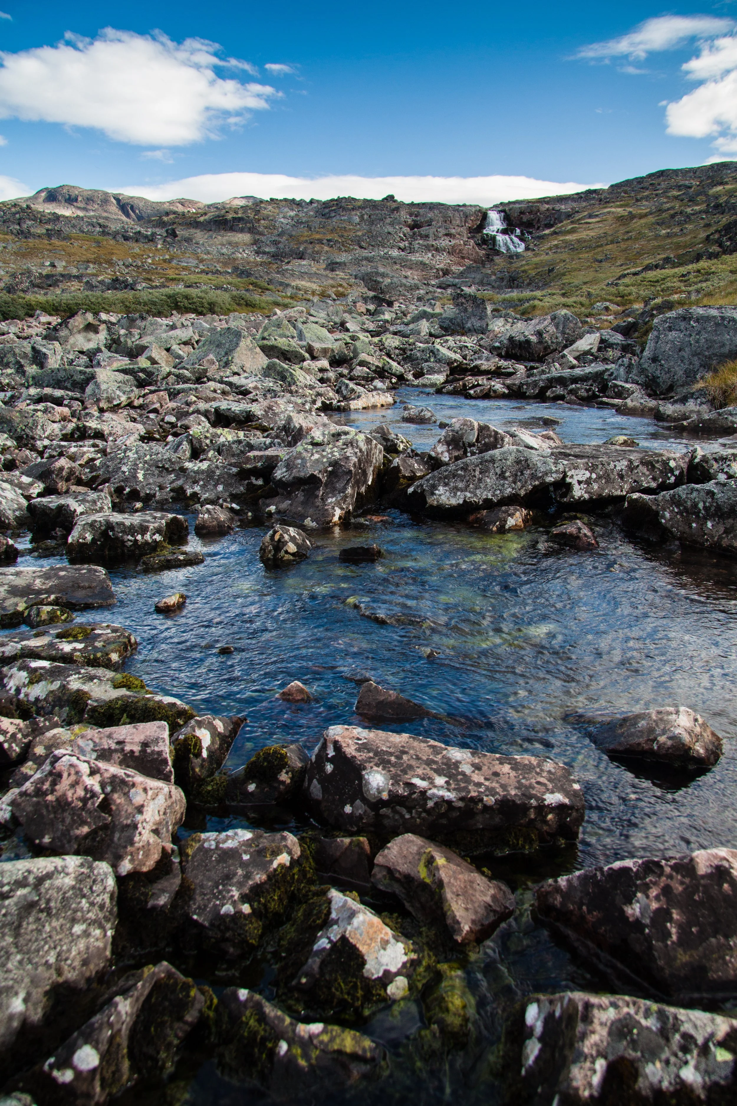 Ein Fluss fließt durch eine felsige Landschaft unter einem blauen Himmel mit wenigen Wolken.