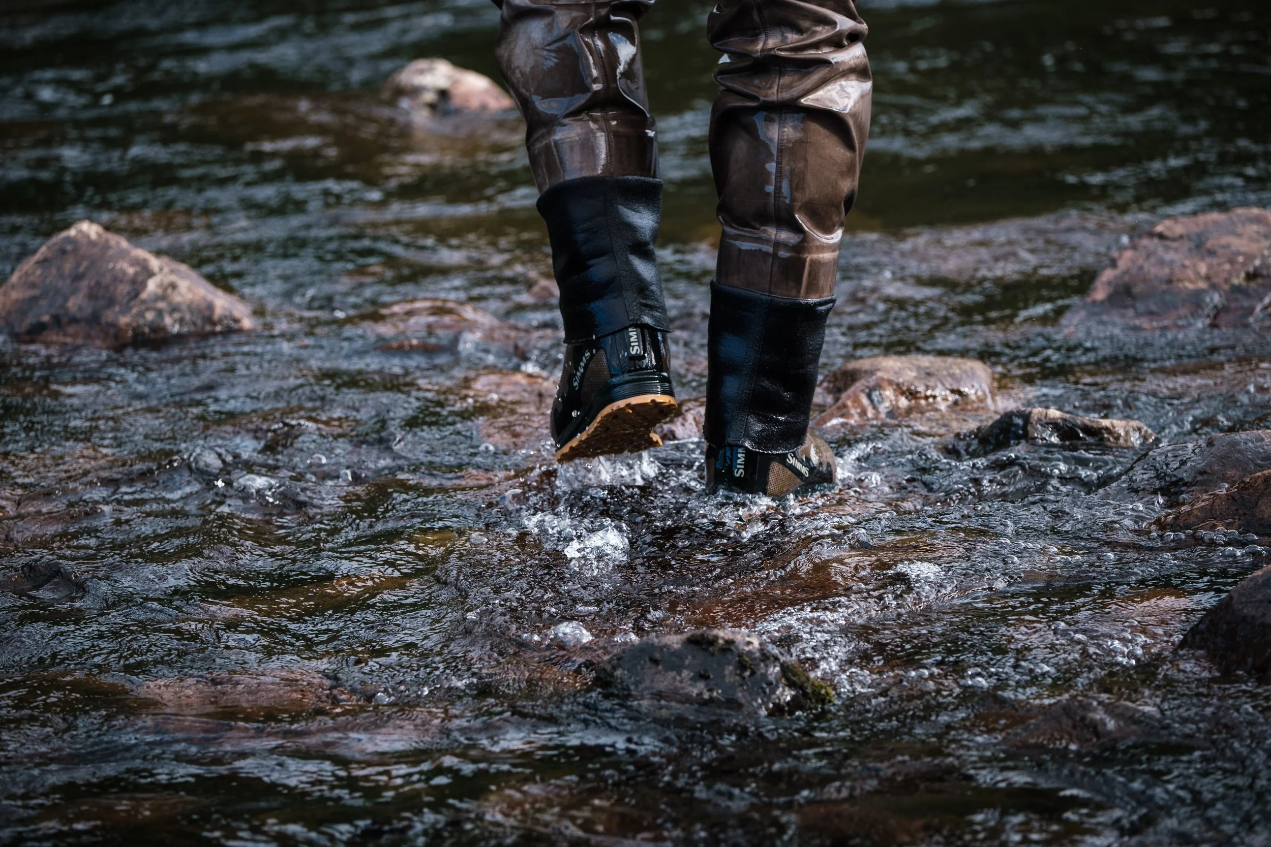 Person, die durch einen Fluss in Gummistiefeln geht.
