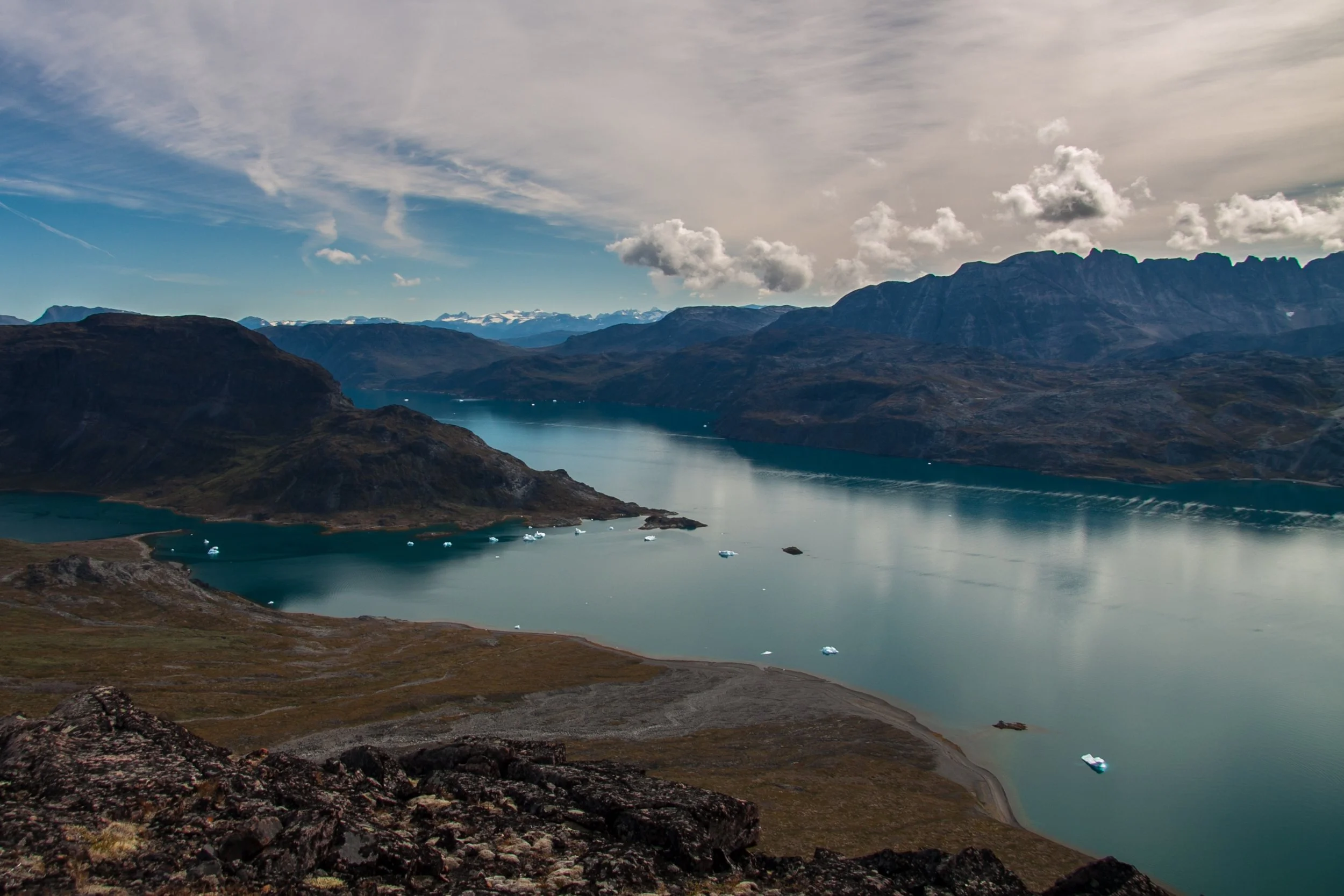 Blick auf einen See mit mehreren Booten, umgeben von Bergen und bewölktem Himmel.