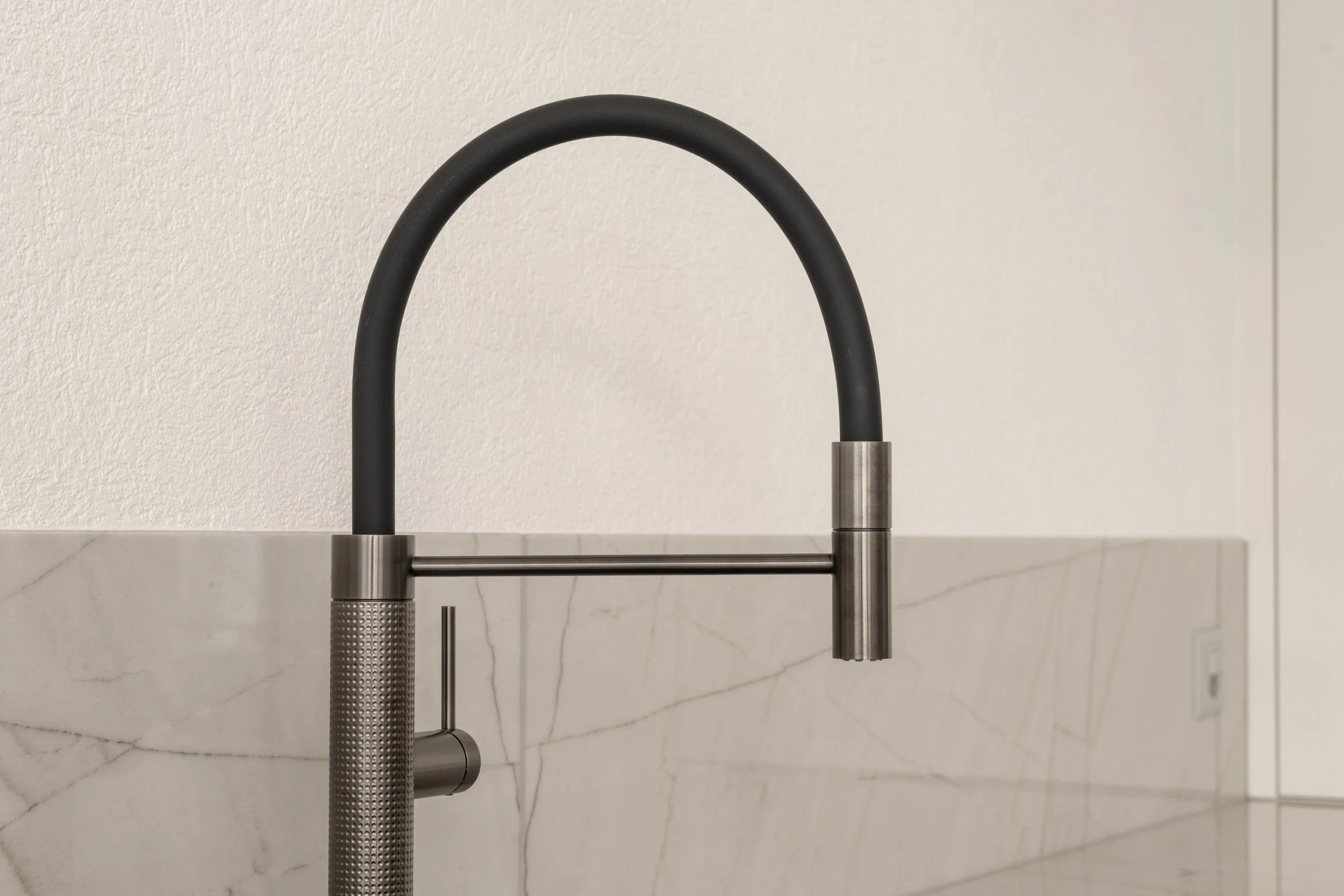 Moderner Küchen Wasserhahn mit schwarzem Schlauch und Edelstahl-Details über einer Küchenarbeitsplatte aus Marmor