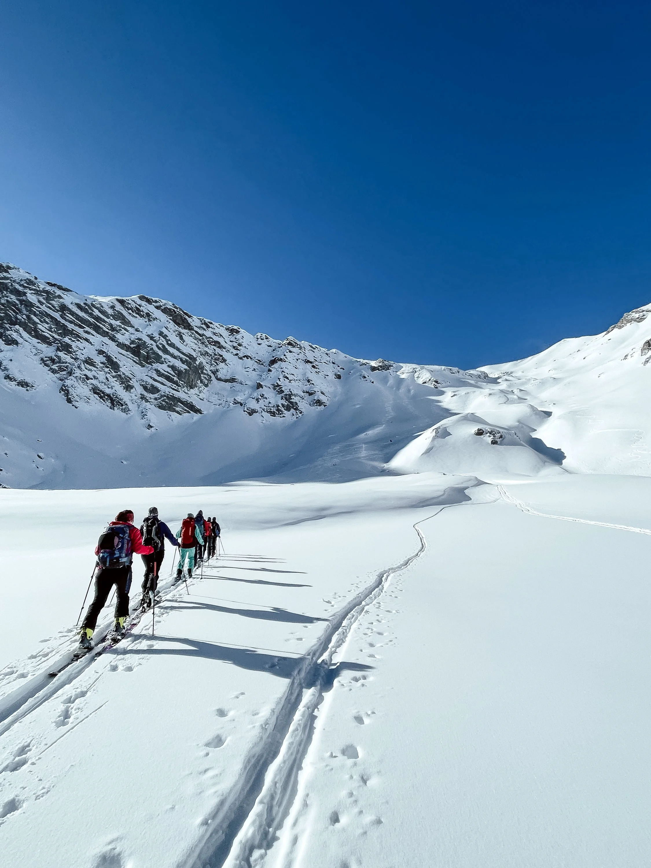 Eine Gruppe von Menschen beim Skitouren in verschneitem Gebirge unter klarem blauen Himmel.